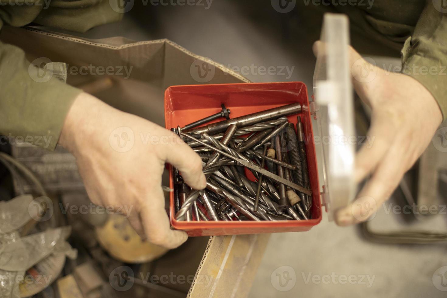 Drill bits in box. Hand holds box of drills. Tools in garage. photo