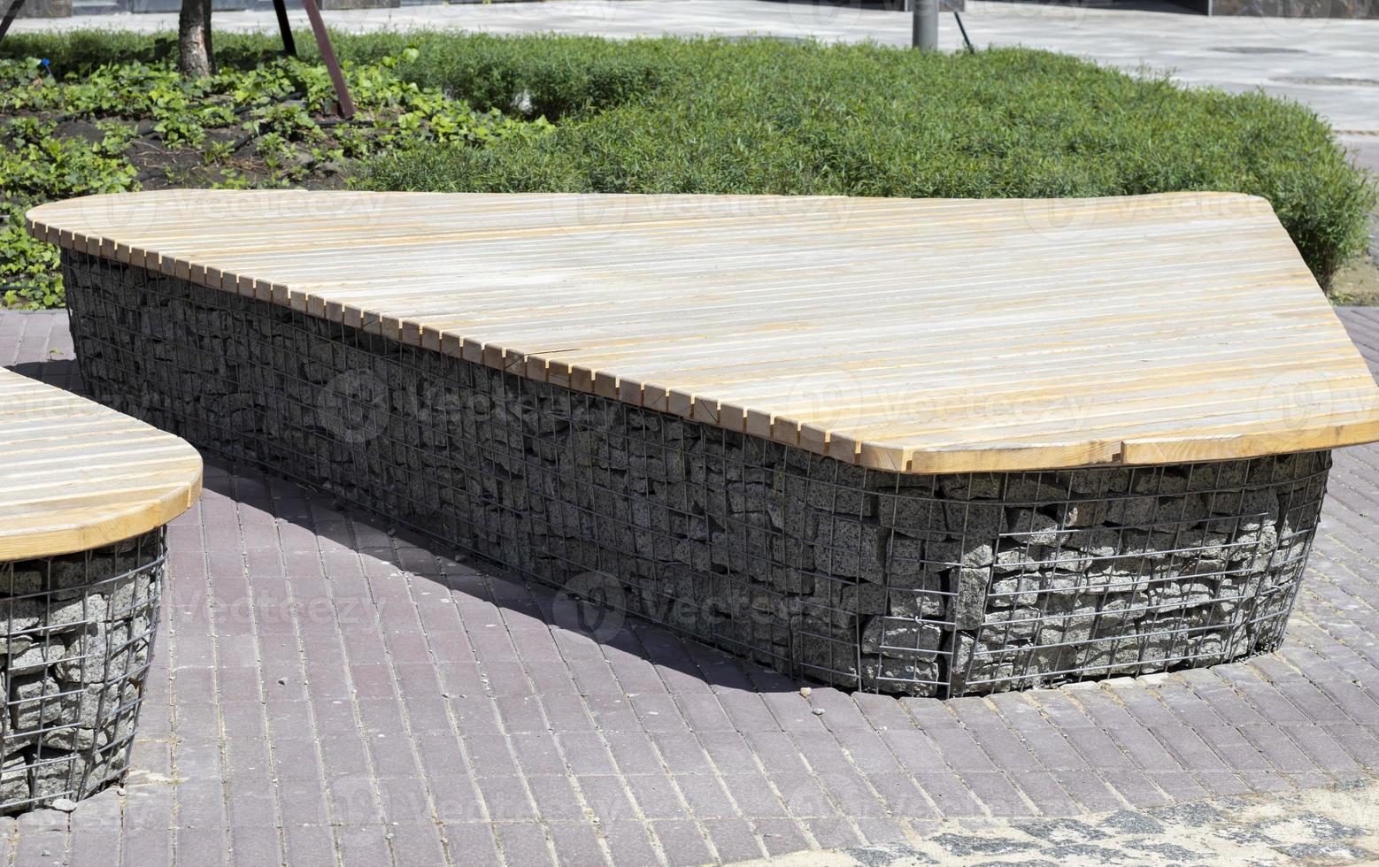 Wooden benches from gabion baskets with stones inside. Wood mounted on gabions. Benches of modern design. Detail of a low wood-topped gabion wall for use as a bench. photo