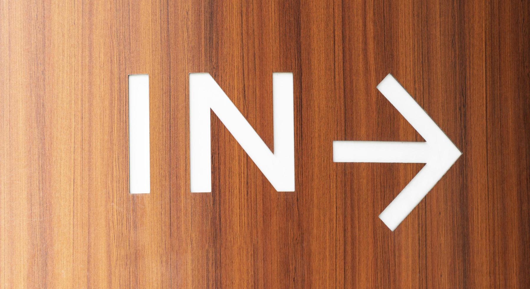 Brown wooden wall with message IN and white arrow photo