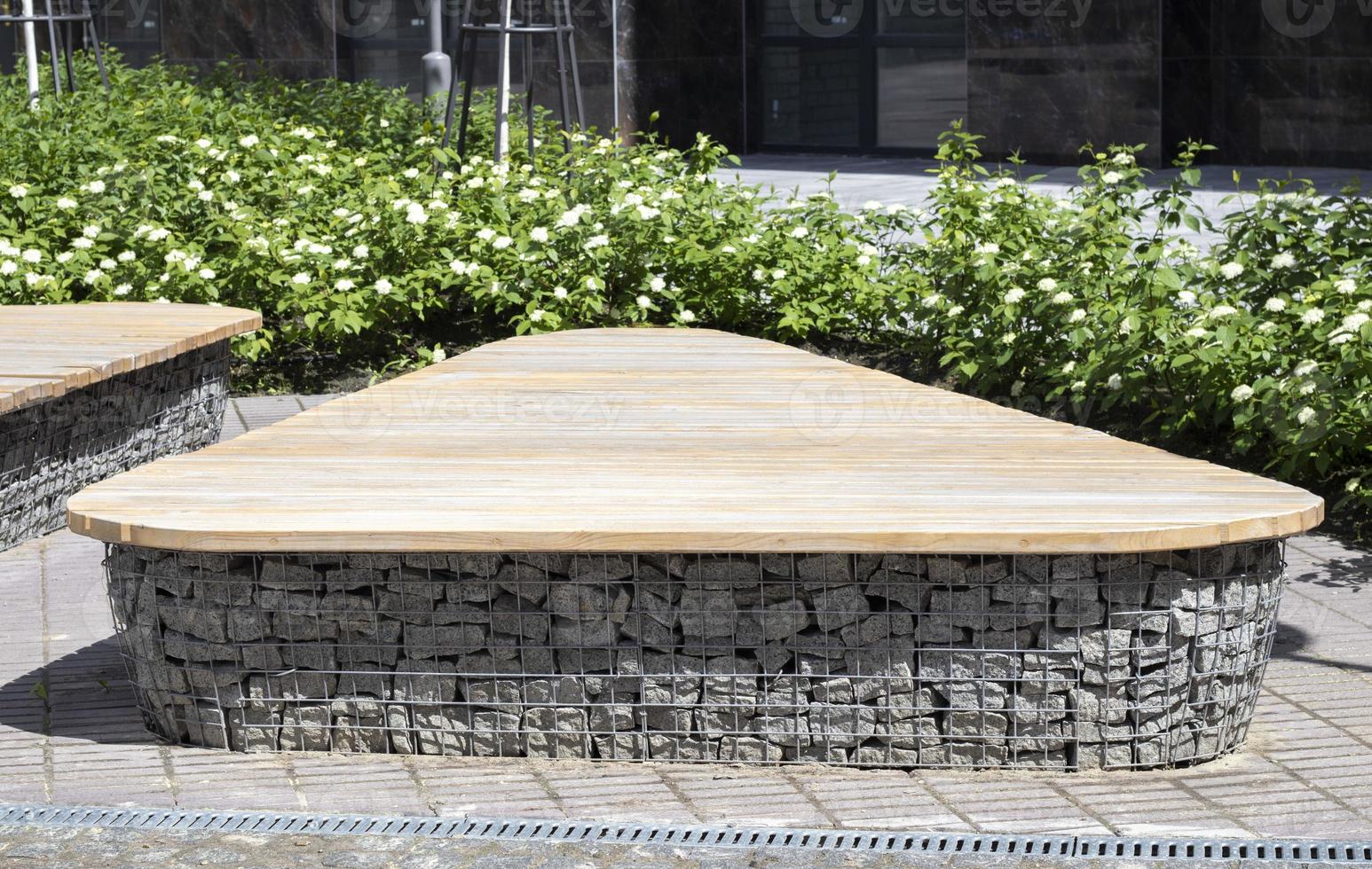 Wooden benches from gabion baskets with stones inside. Wood mounted on gabions. Benches of modern design. Detail of a low wood-topped gabion wall for use as a bench. photo