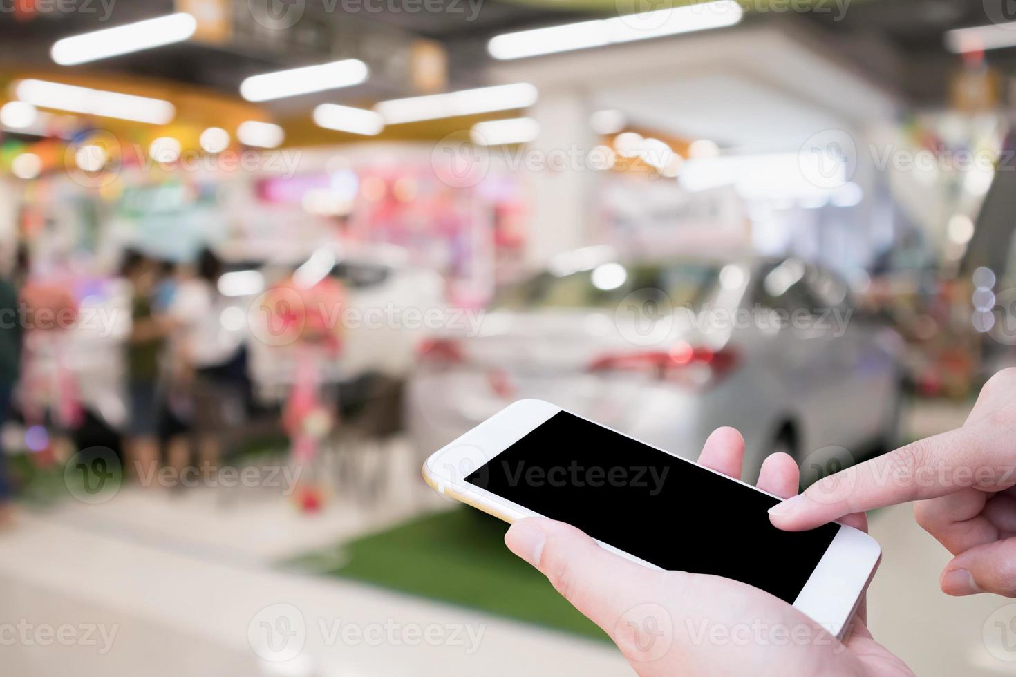 Hand hold smartphone with Abstract blur car showroom top view defocused background photo