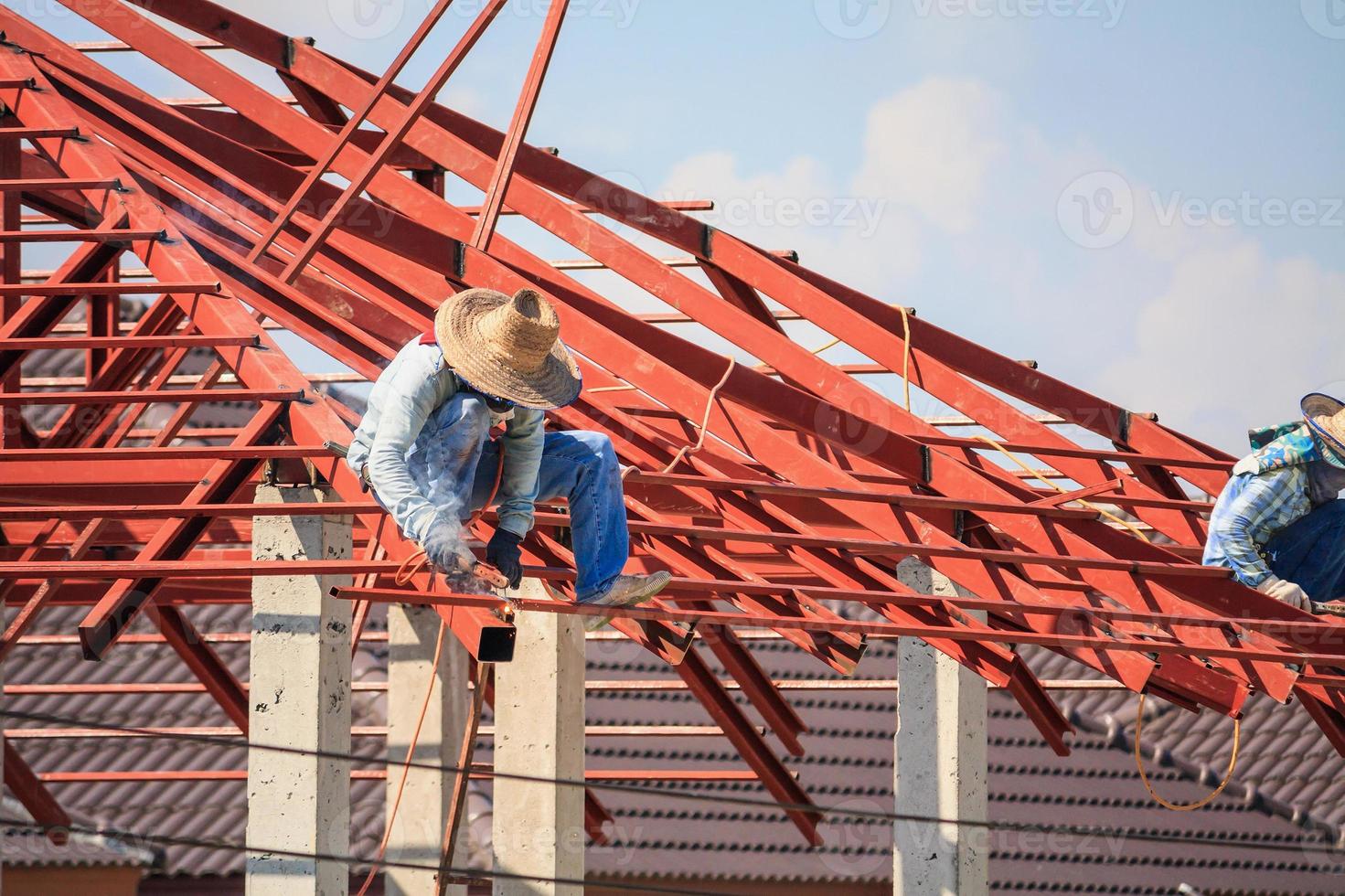 welder workers installing steel frame structure of the house roof at building construction site photo