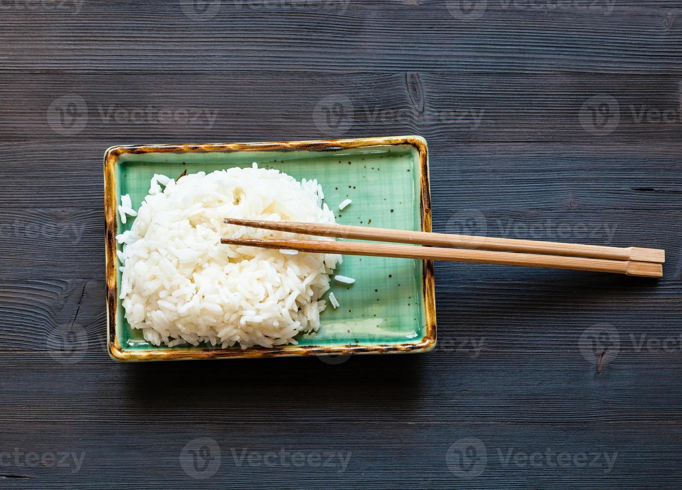 boiled rice with chopsticks on plate on dark table photo