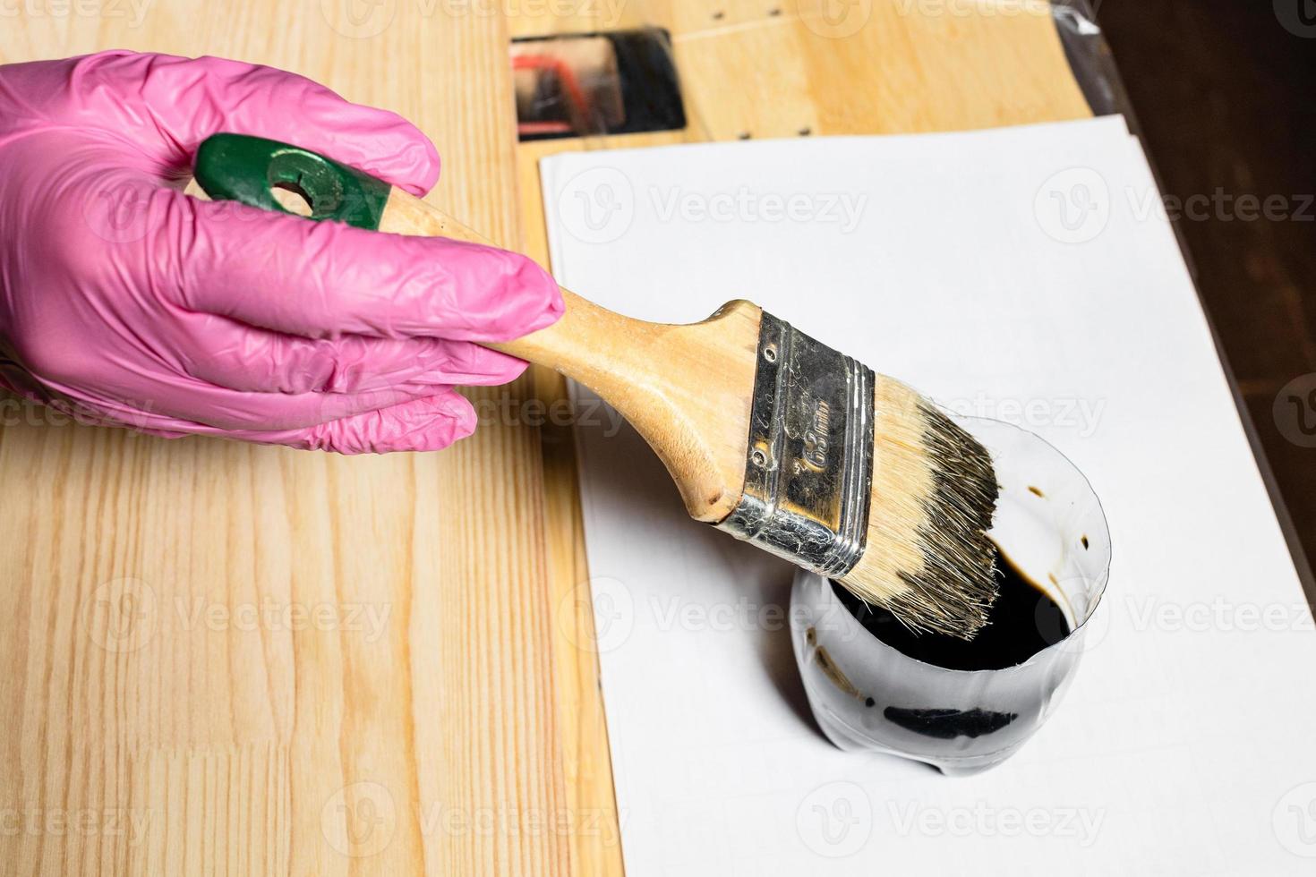 mano enguantada sumerge el cepillo en un frasco de tinte para madera foto