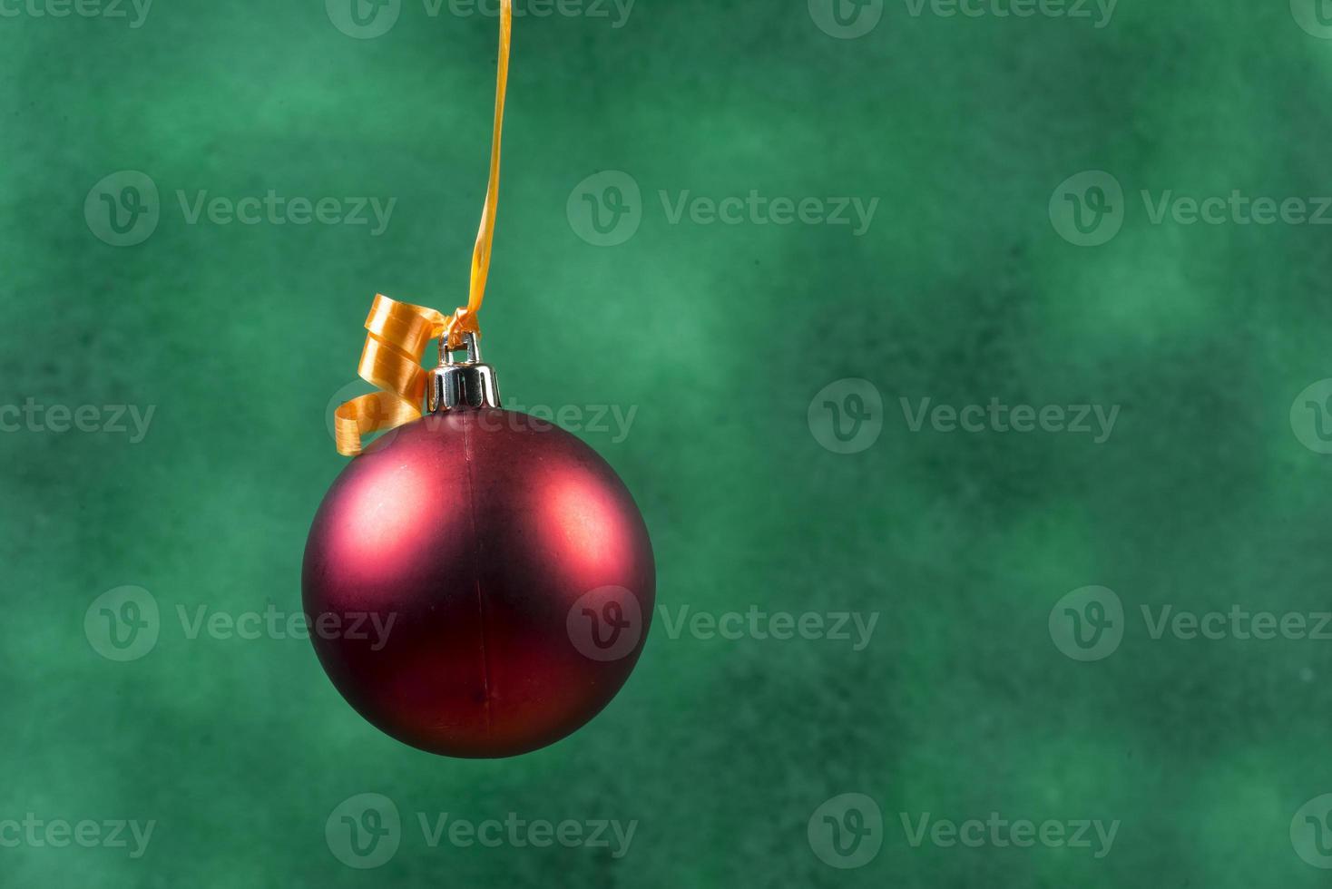 red christmas ball hanging with orange ribbon on green background photo