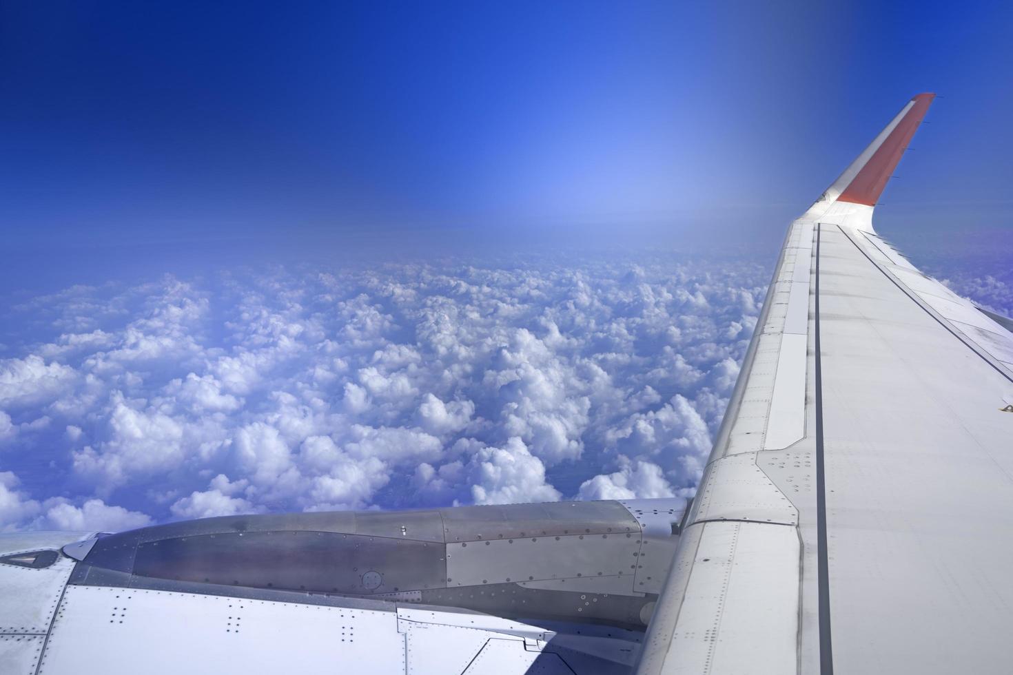 airplane wings in the cloudy sky A plane flying above the beautiful scenery of white fluffy clouds in the blue sky. photo