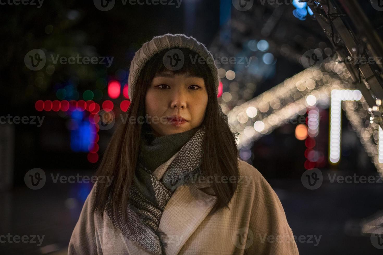 A young beautiful fashionable Korean woman in a hat and coat walks through the Christmas streets of the city in the evening. photo