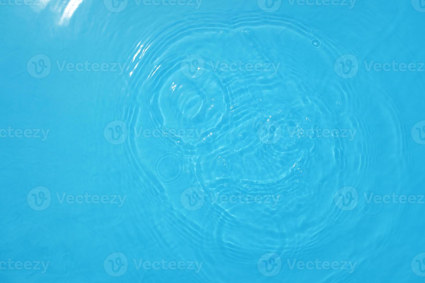 Defocus blurred transparent blue colored clear calm water surface texture with splashes and bubble. Trendy abstract nature background. Water wave in sunlight with copy space. Blue watercolor shining. photo