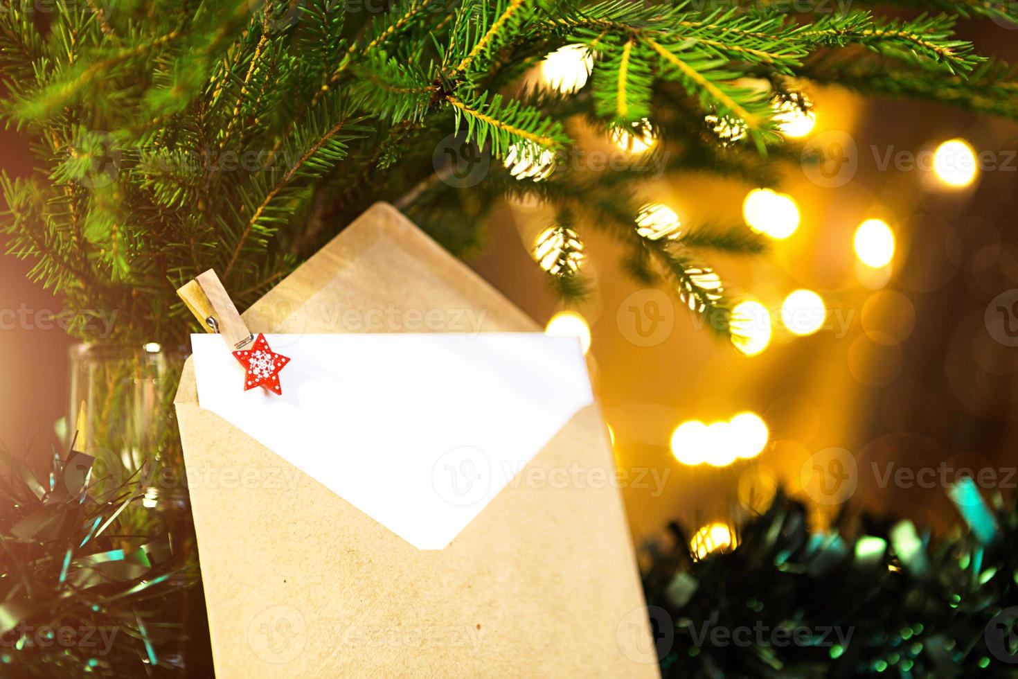 Envelope with sheet of paper- letter to Santa Claus, Copy space on a Christmas background of defocus lights in bokeh, garlands, fir branches. Clothespin-star. New year, wish list, dream, gifts photo