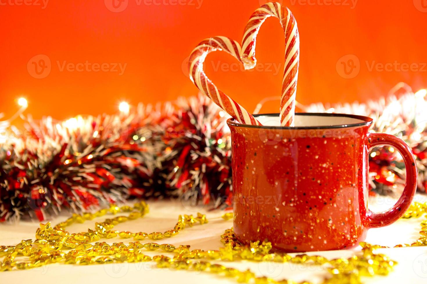 Red mug with striped candy canes in the shape of a heart on a red Christmas background with lights of garlands in bokeh. Copy space. New Year. photo