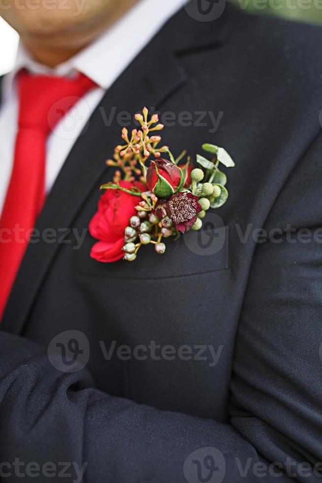 The groom's wedding boutonniere of succulents and red flowers in a black jacket with a red tie. Festive decor, flowers, attire for the marriage registration. Close-up, space for text photo