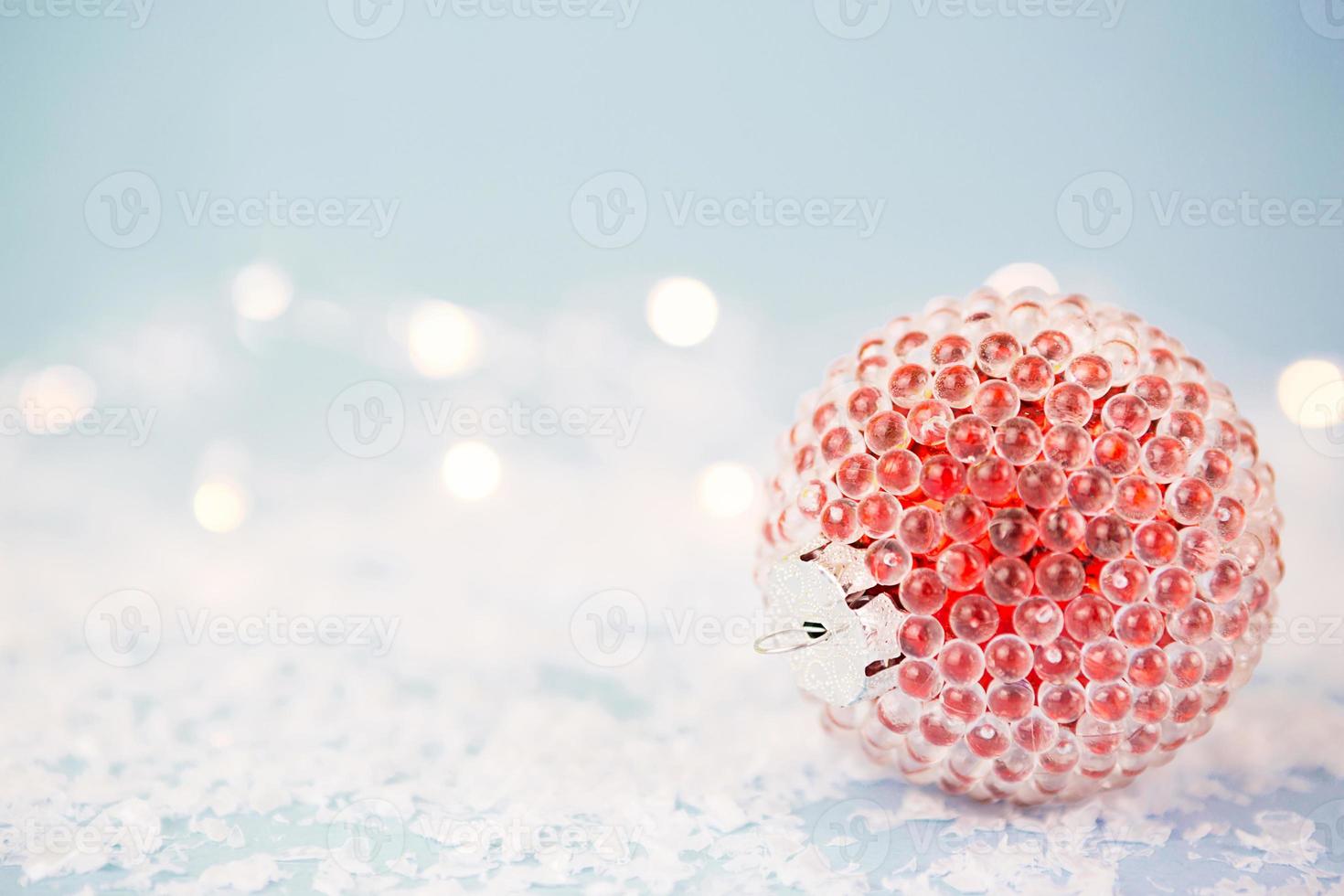 Red Christmas ball on a blue background with artificial snow and lights of garlands in bokeh. Festive background, new year. Copy space photo