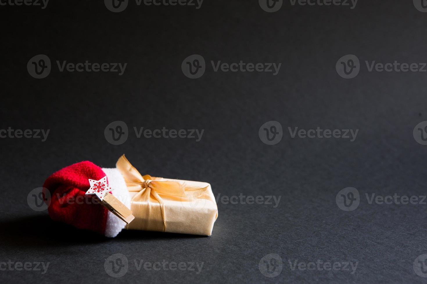 A box with a Christmas gift in a package tied with a ribbon and with a Santa hat on a black background. Black Friday, buying gifts for the new year. Space for text photo
