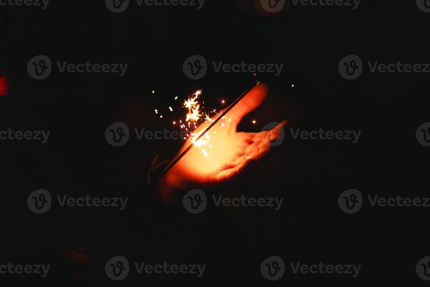 Sparks and light from sparklers in the dark on the palm of a person. Christmas magic, new year's eve, festive background. Space for text photo