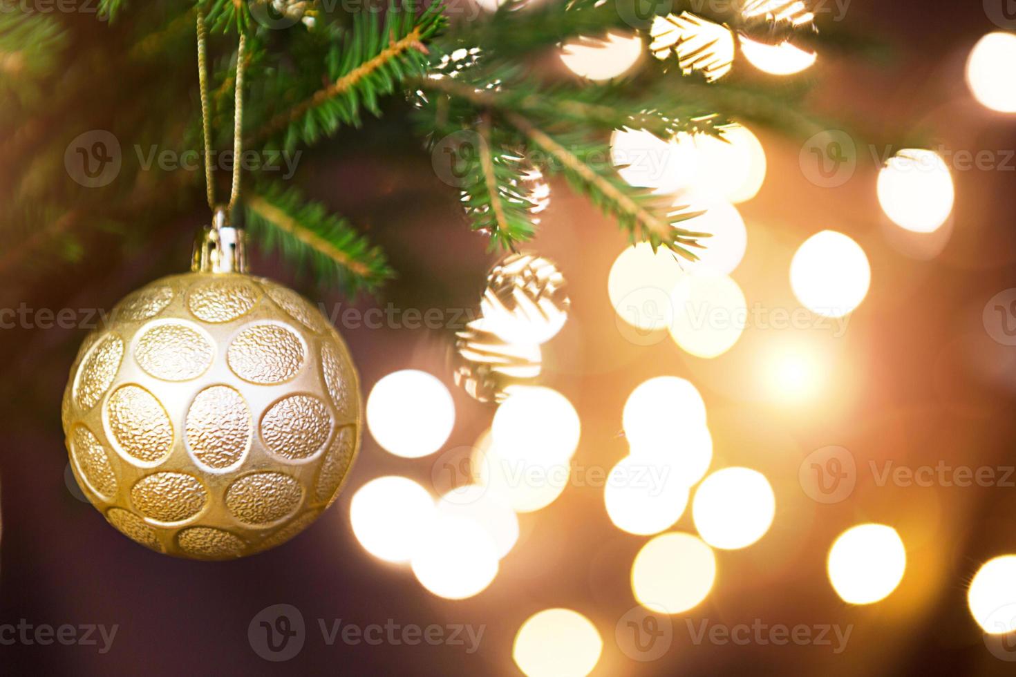 Golden Christmas ball on a live branch of a fir tree with Golden lights of garlands in defocus. New year, Christmas, holiday background, bokeh, copy space photo