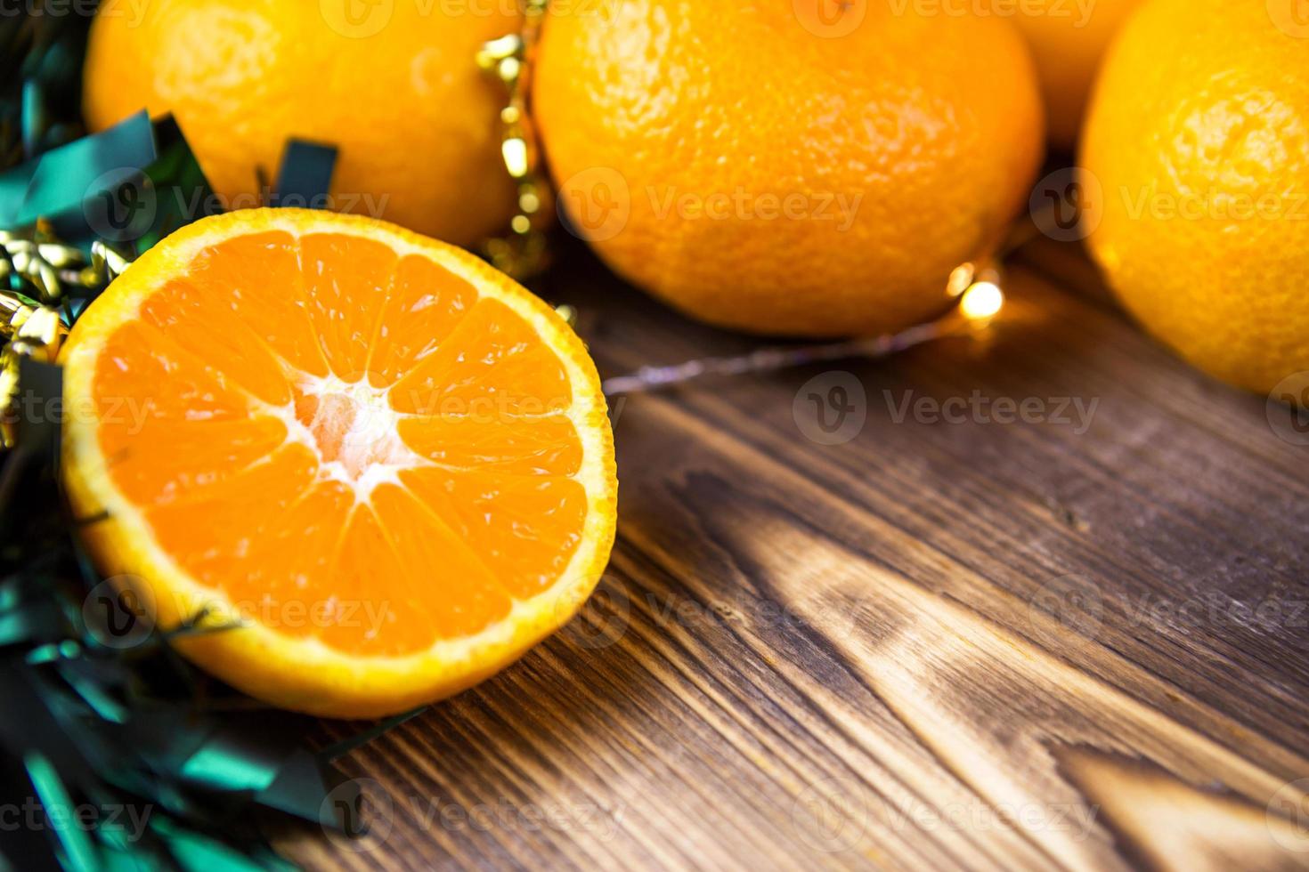 New year's holiday background made of wood with tangerines, garland lights and green tinsel. Half of an orange, citrus aroma of the holiday. Christmas, New year. Space for text. Frame photo