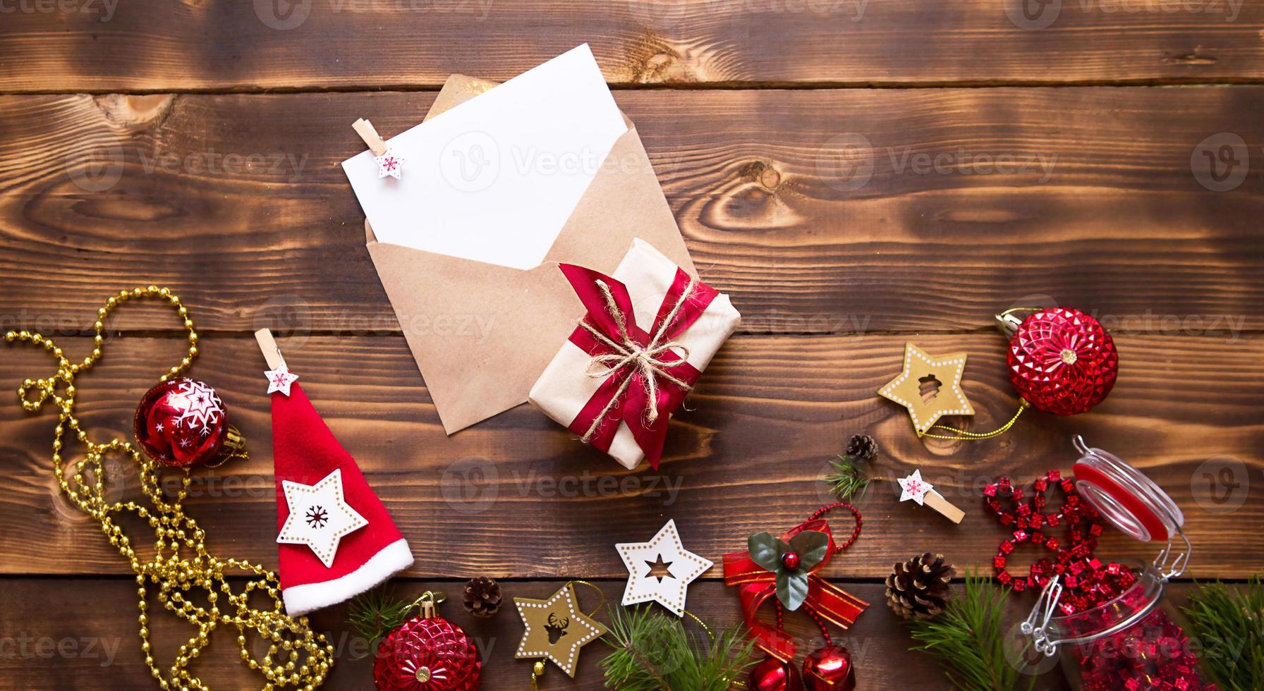 Mail envelope made of craft paper with a white sheet for text on a wooden background with Christmas decor. A letter to Santa Claus, a wish list, a new year's dream, a gift. Flat lay, copy space photo