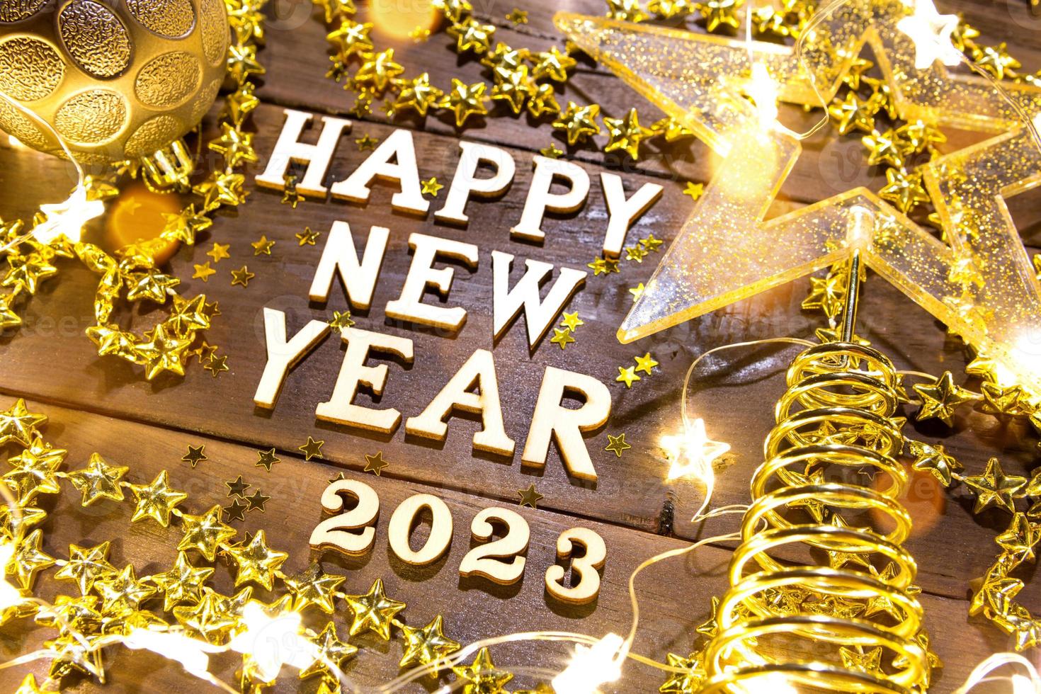 feliz año nuevo, letras de madera y los números 2023 en un fondo festivo con lentejuelas, estrellas, purpurina, luces de guirnaldas. saludos, postal. calendario, portada foto