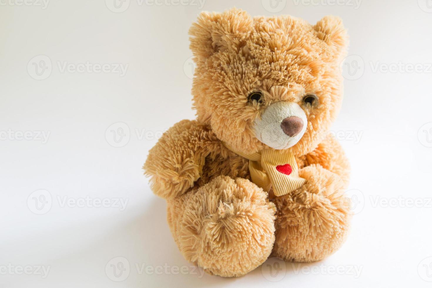 Soft Teddy bear with long light brown fur and a red heart on a scarf around his neck. Valentine's day gift, children's toy. White background, space for text photo