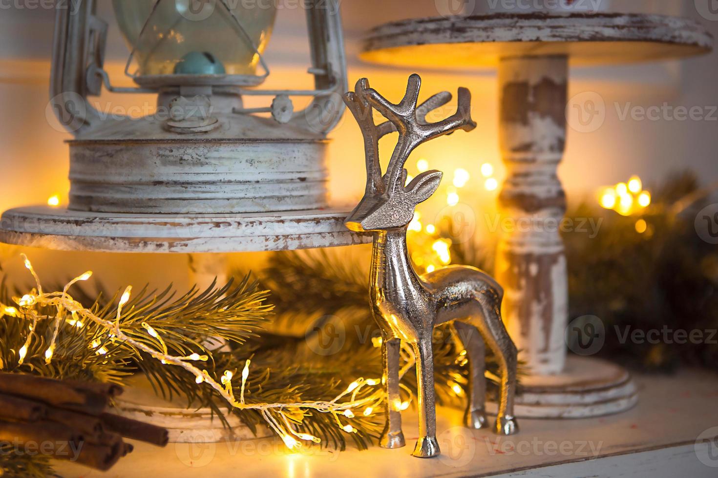 Christmas Decoration silver figure of a deer with branching horns, cinnamon sticks in festive lights garland yellow. New year, Christmas tree branch, white antique rustic decor. Copy space photo