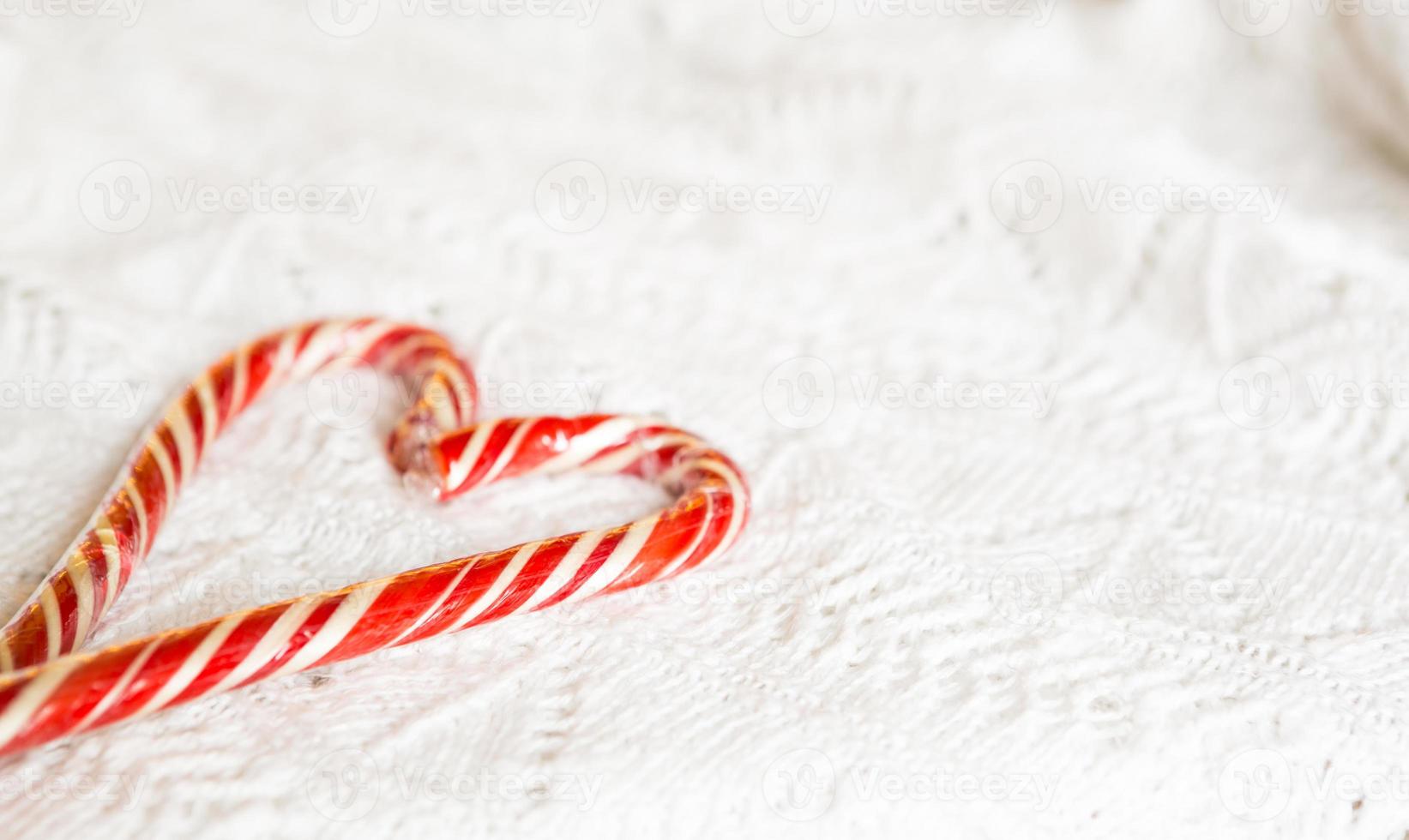 Christmas candy cane striped Santa in the form of heart on a white knitted blanket. A symbol of love, a gift to a loved one, a sweet treat. New Year. Space for text photo