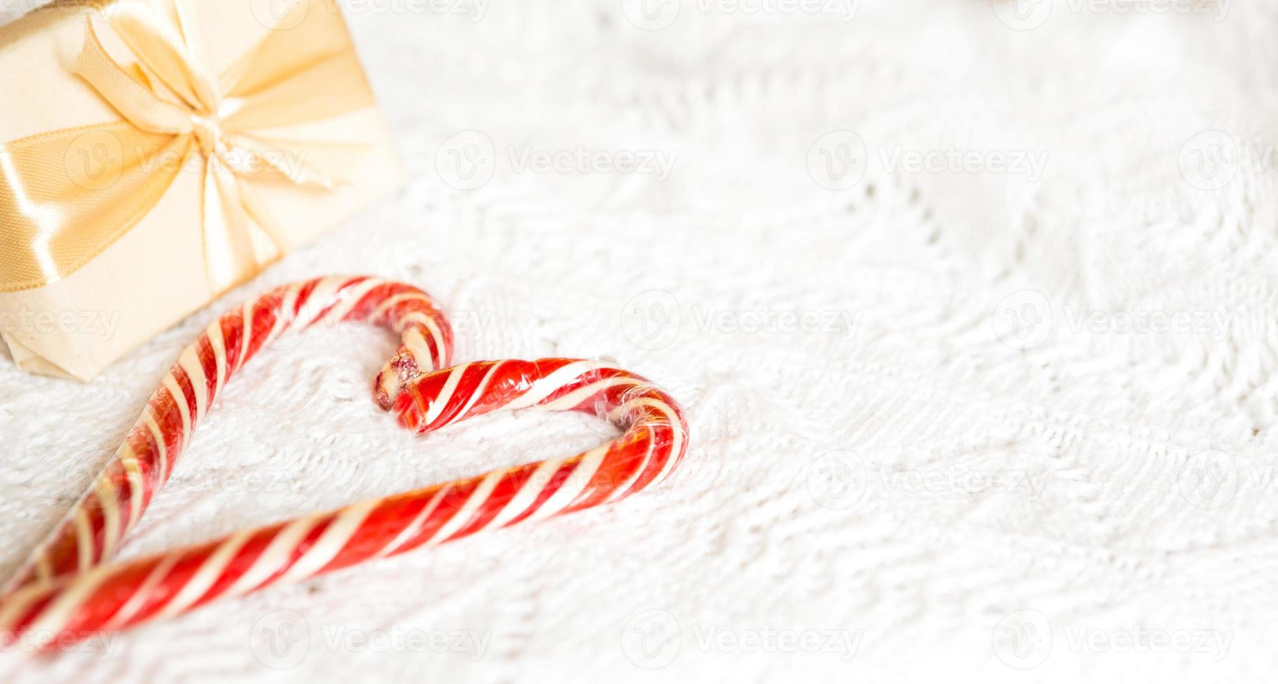 Christmas candy cane striped Santa in the form of heart on a white knitted blanket. A symbol of love, a gift to a loved one, a sweet treat. New Year. Space for text photo