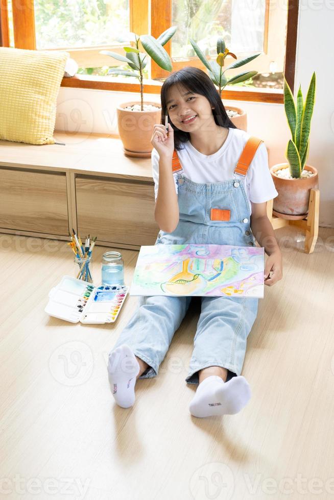 Young girl sitting on the floor and painting on paper at home. Hobby and art study at home. photo