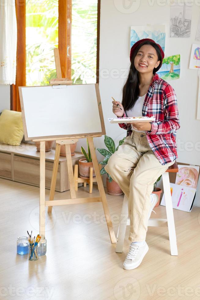 Young girl sitting on a chair with easel for drawing hold Color palette and brush in the room. photo