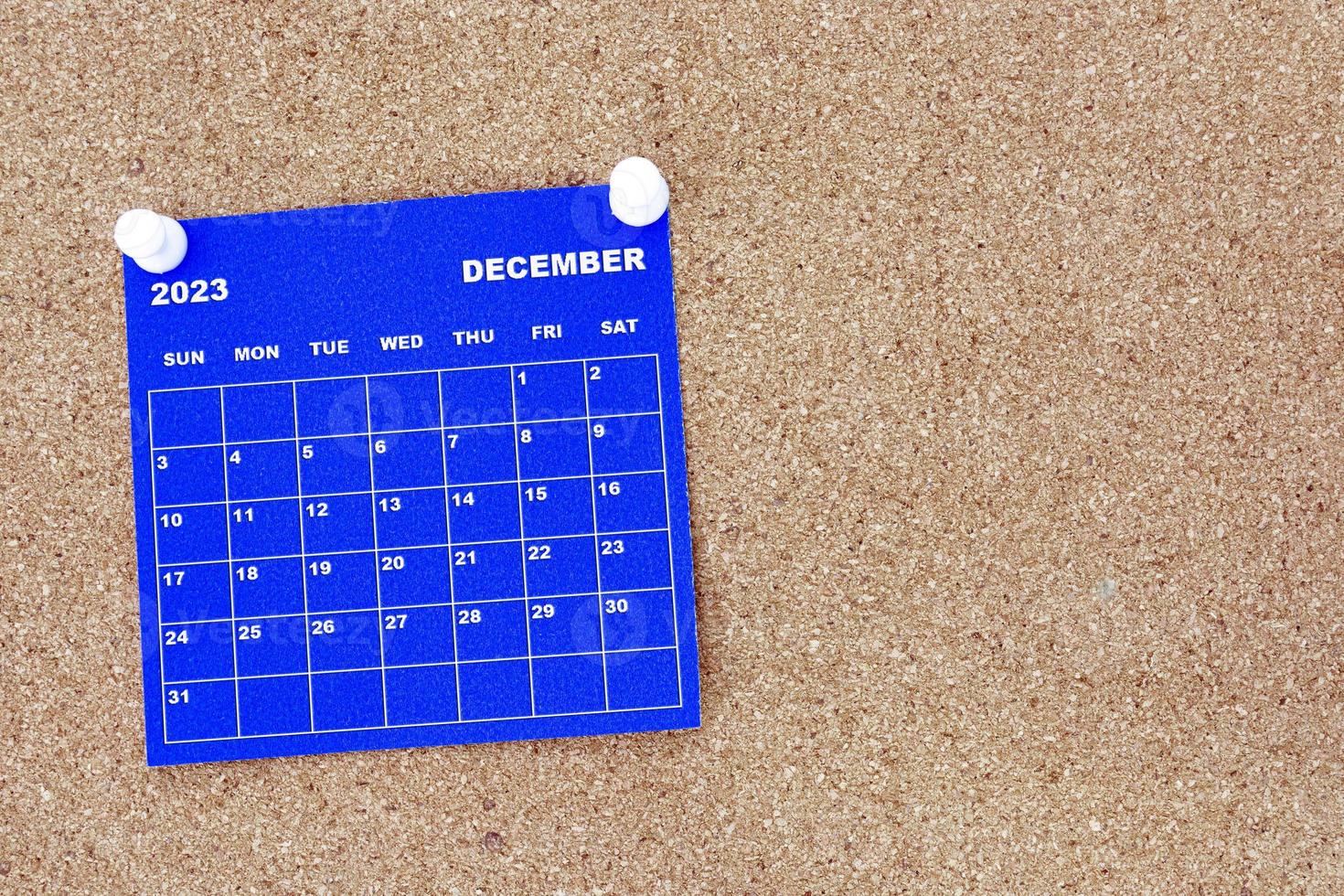 December 2023 blue calendar with pin on cork bulletin billboard. photo