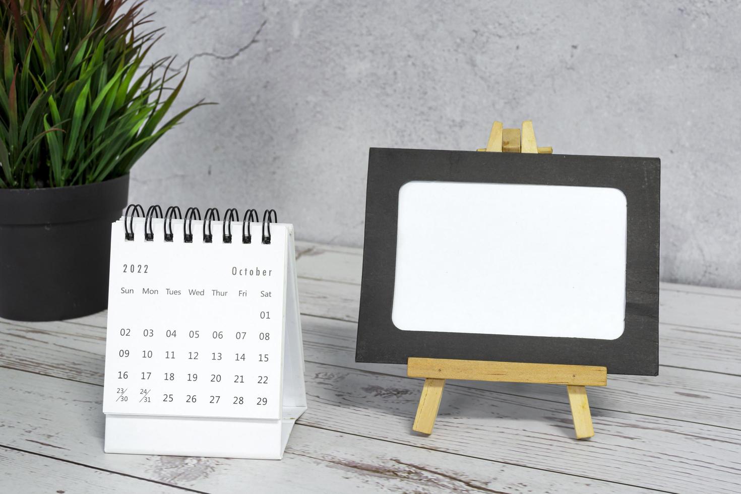 White October 2022 calendar on wooden desk with paper frame and potted plant. photo