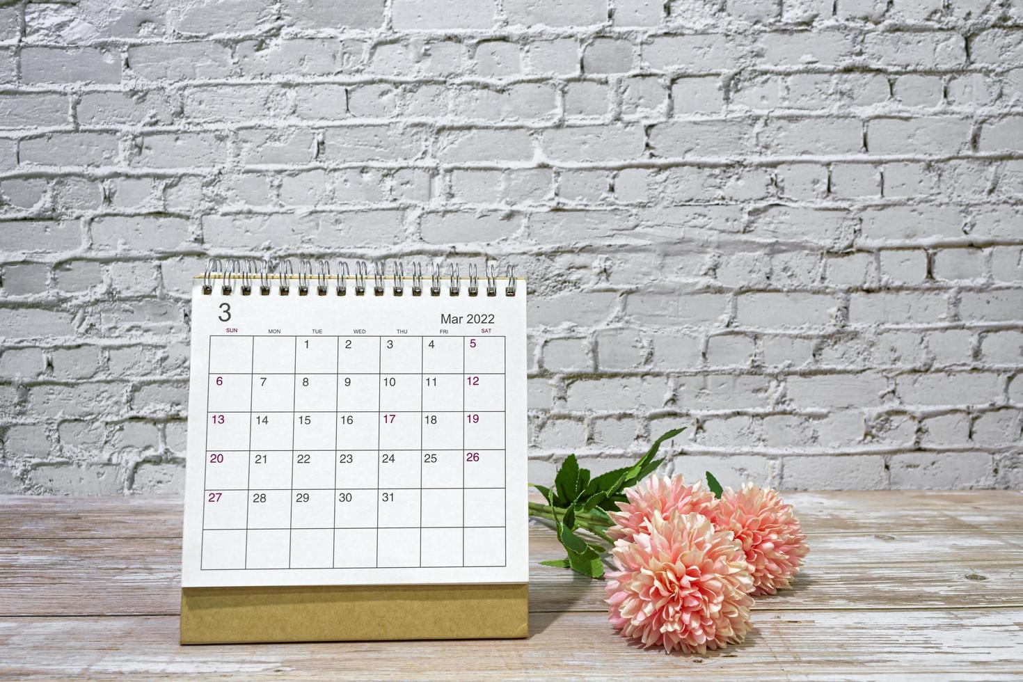 March 2022 white calendar with flowers on wooden desk. Copy space. photo