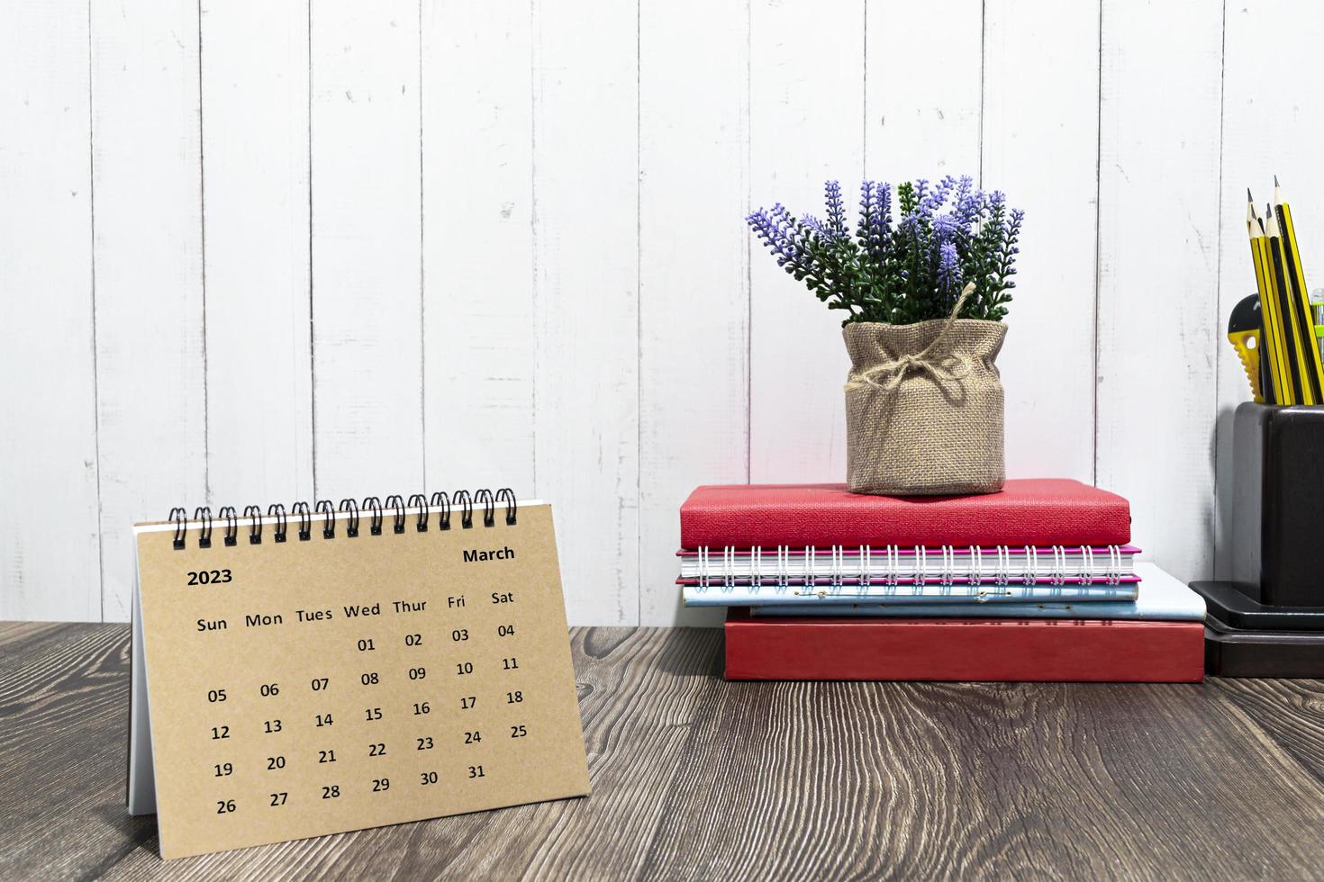 Brown March 2023 calendar on wooden desk with office stationery. photo