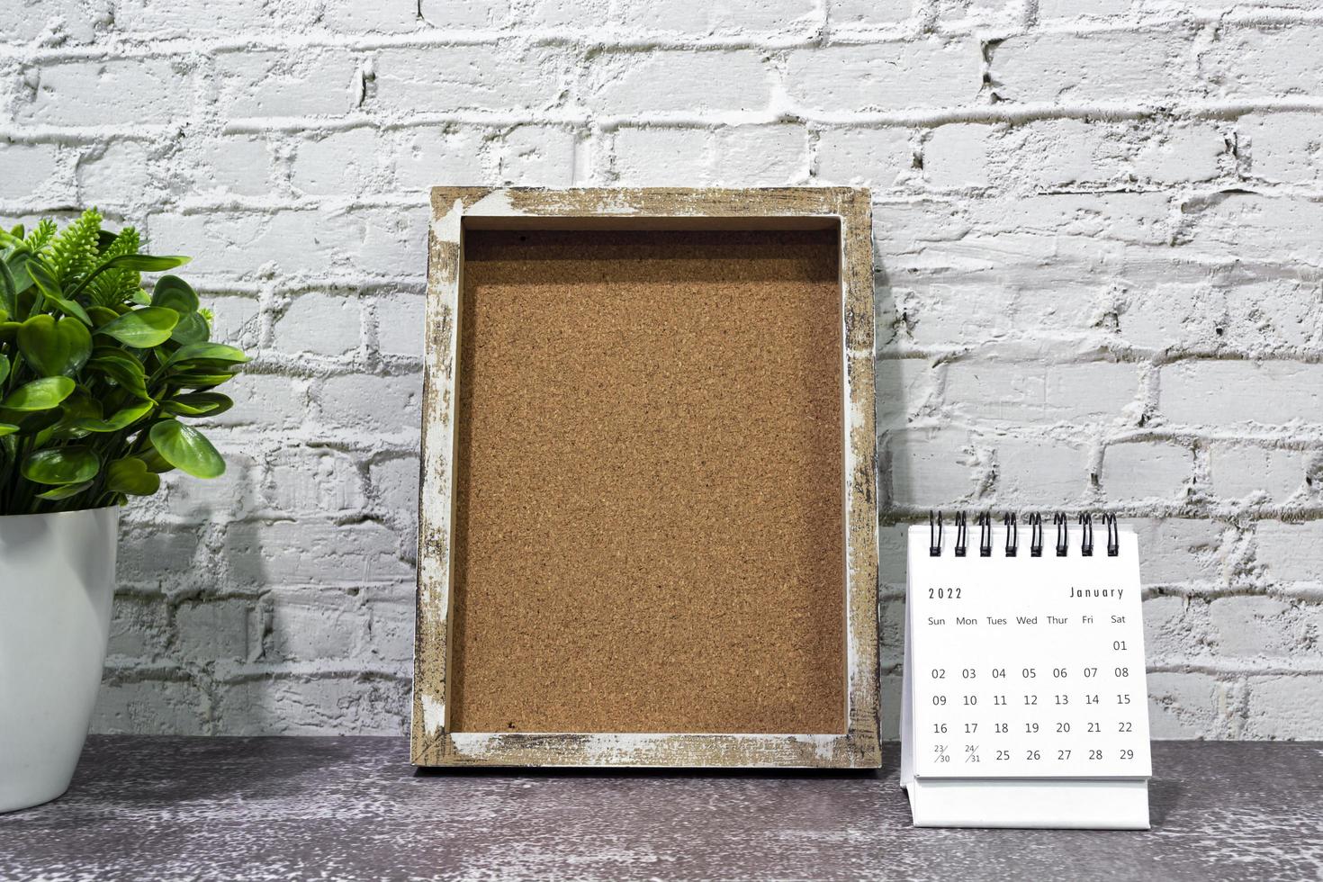 January 2022 white calendar with wooden frame and potted plant on wooden desk. photo