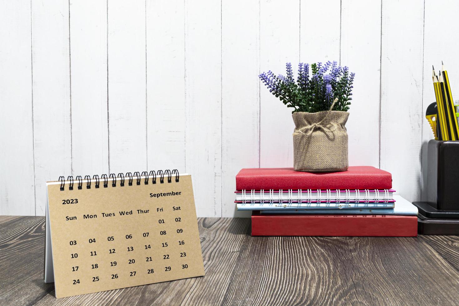 Brown September 2023 calendar on wooden desk with office stationery. photo