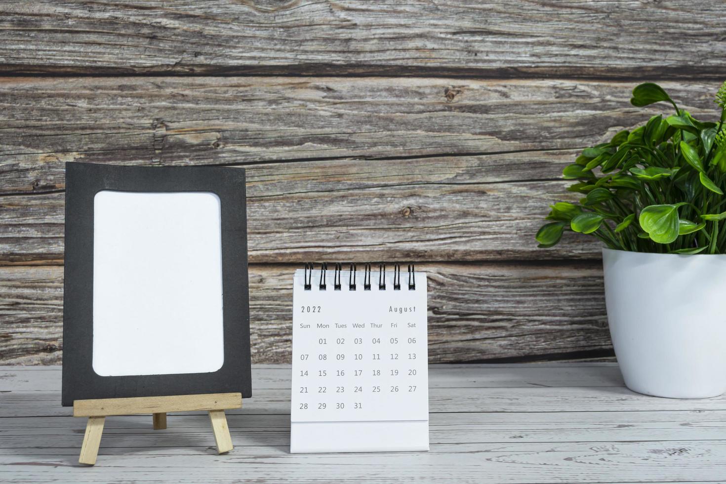 White August 2022 calendar on wooden desk with paper frame and potted plant. photo