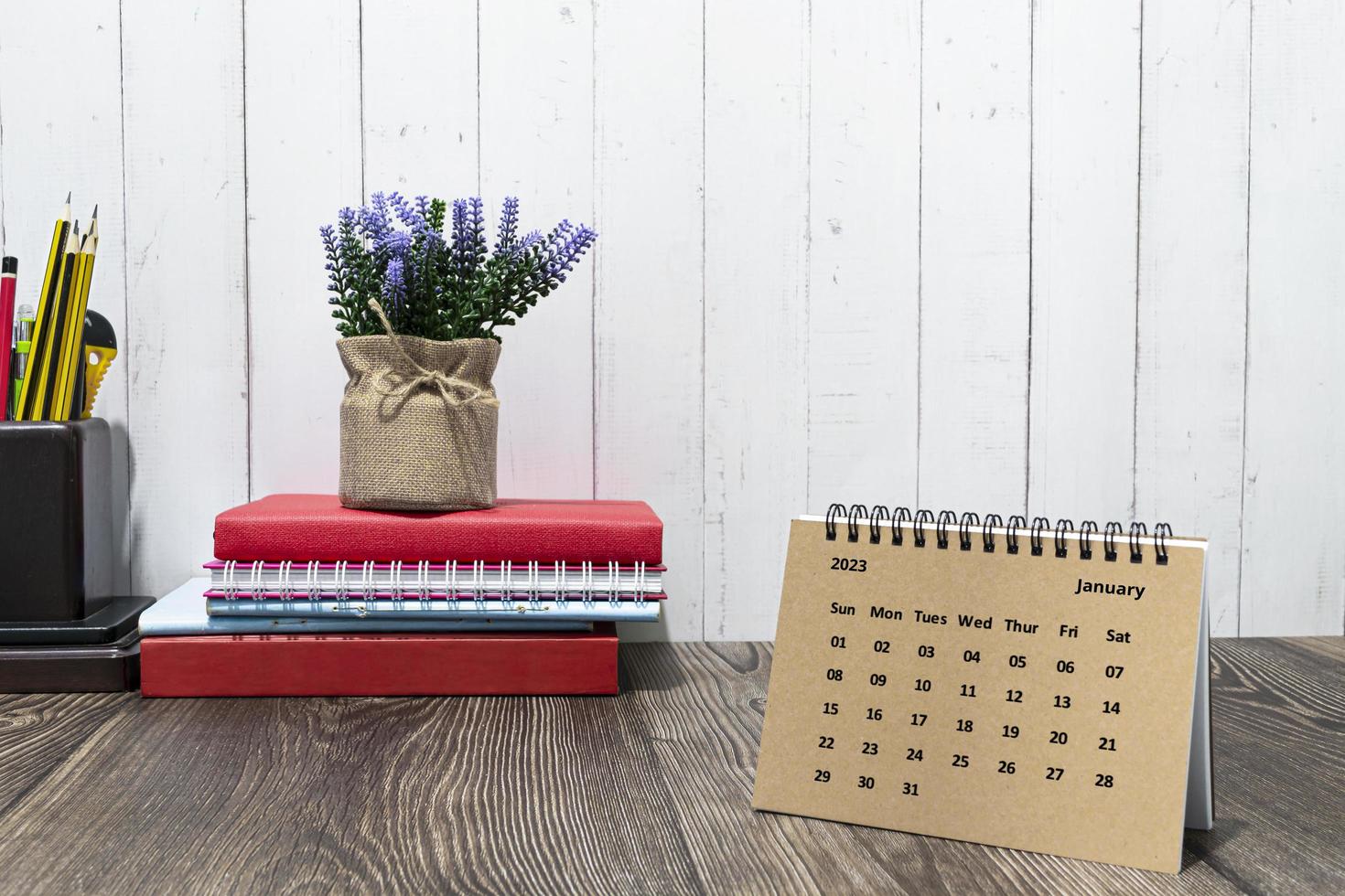 Brown January 2023 calendar on wooden desk with office stationery