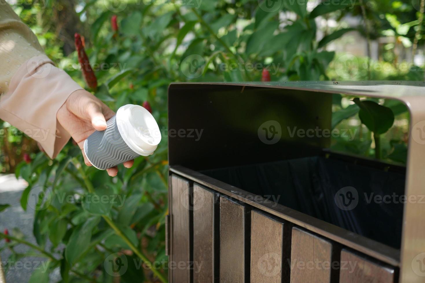 women hand throwing an empty coffee paper cup in the garbage trash or bin photo