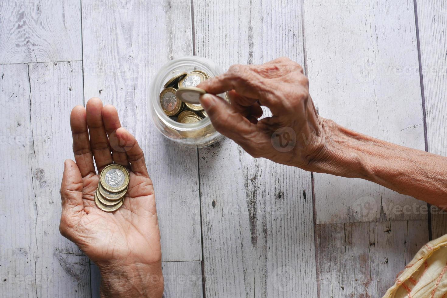 vista superior de la mano de las mujeres mayores ahorrando monedas en un frasco foto