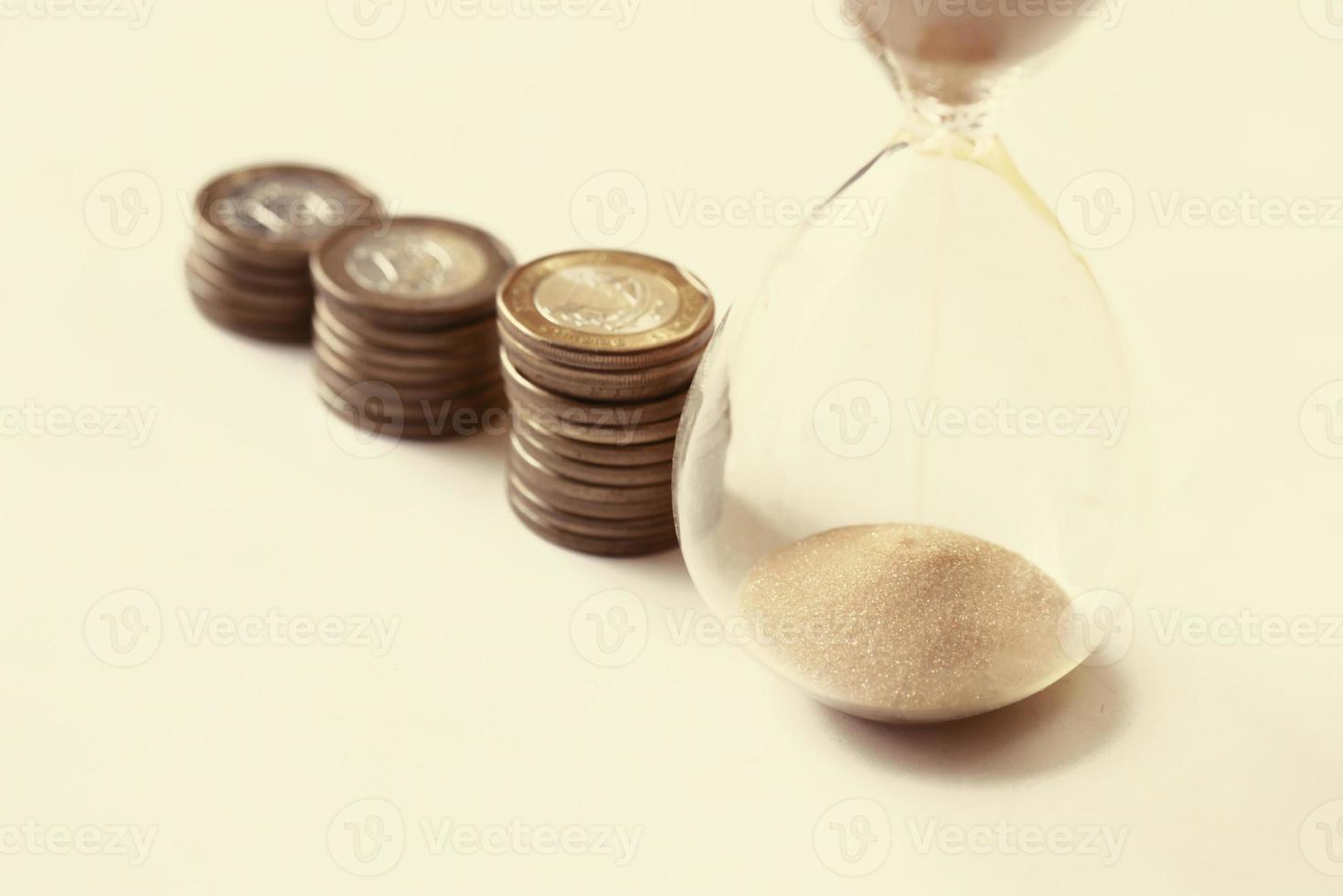 hourglass and stack of coins on table, photo