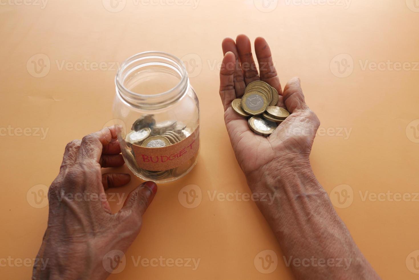 Close up of senior women hand saving coins in a jar photo