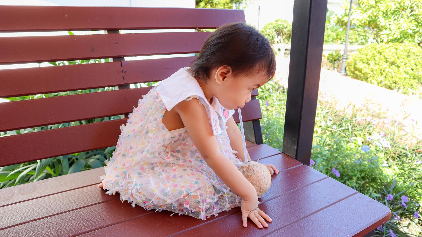 encantadora niña tailandesa asiática de 3 años bebiendo jugo de coco de paja. foto