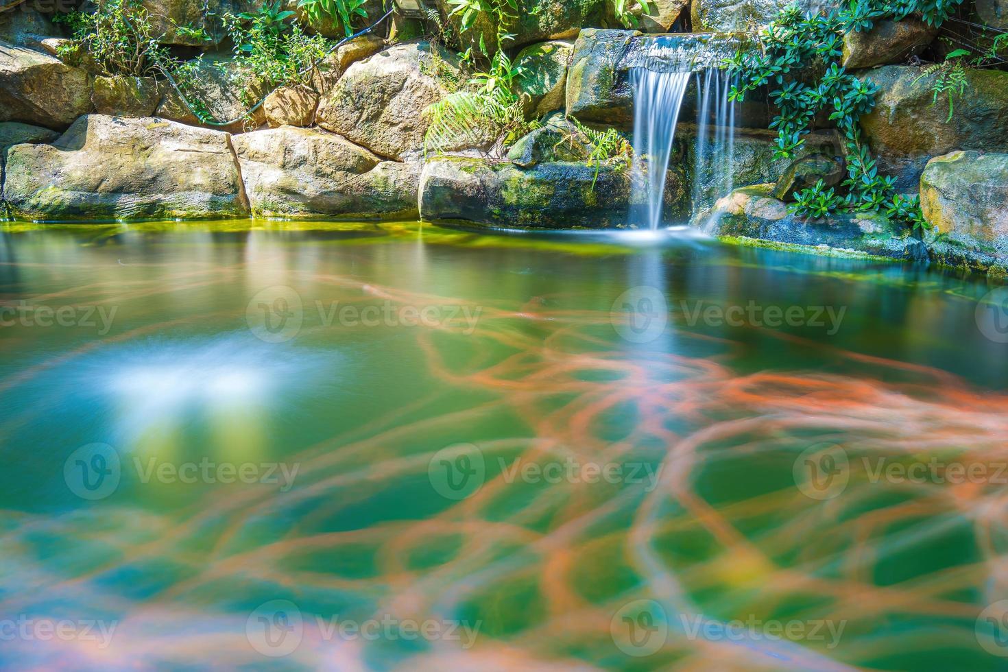 Japanese garden waterfalls. Lush green tropical Koi pond with waterfall from each side. A lush green garden with waterfall cascading down the rocky stones. Zen and peaceful background. photo