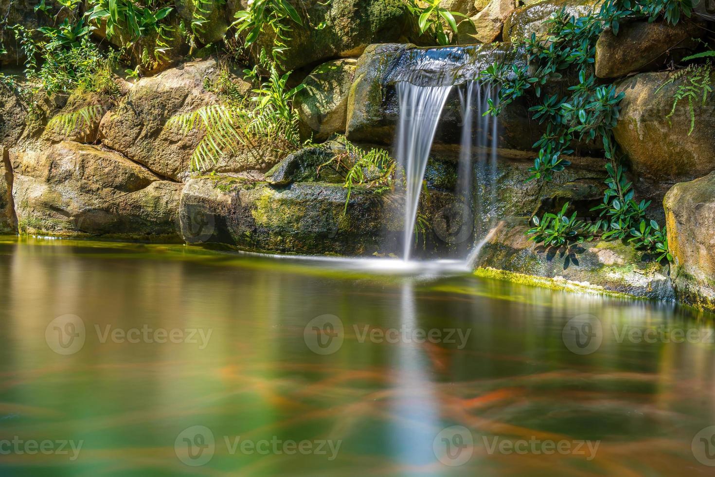Japanese garden waterfalls. Lush green tropical Koi pond with waterfall from each side. A lush green garden with waterfall cascading down the rocky stones. Zen and peaceful background. photo