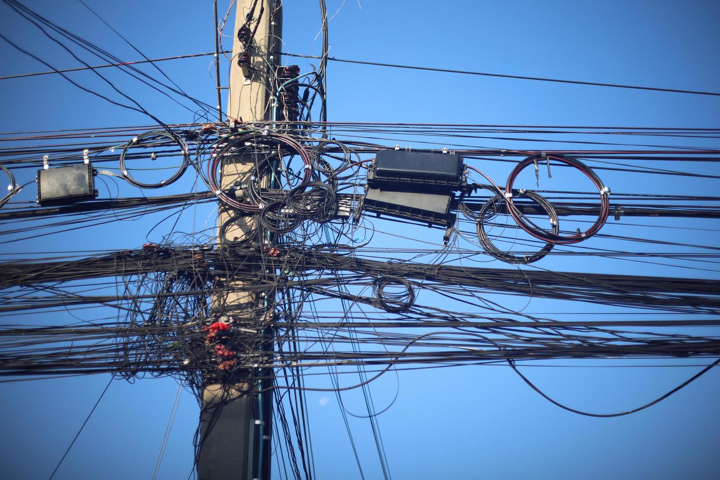 muchos cables eléctricos y de comunicación están enredados en un lío en los postes de energía. concepto confuso e inseguro para operar y administrar el sistema foto