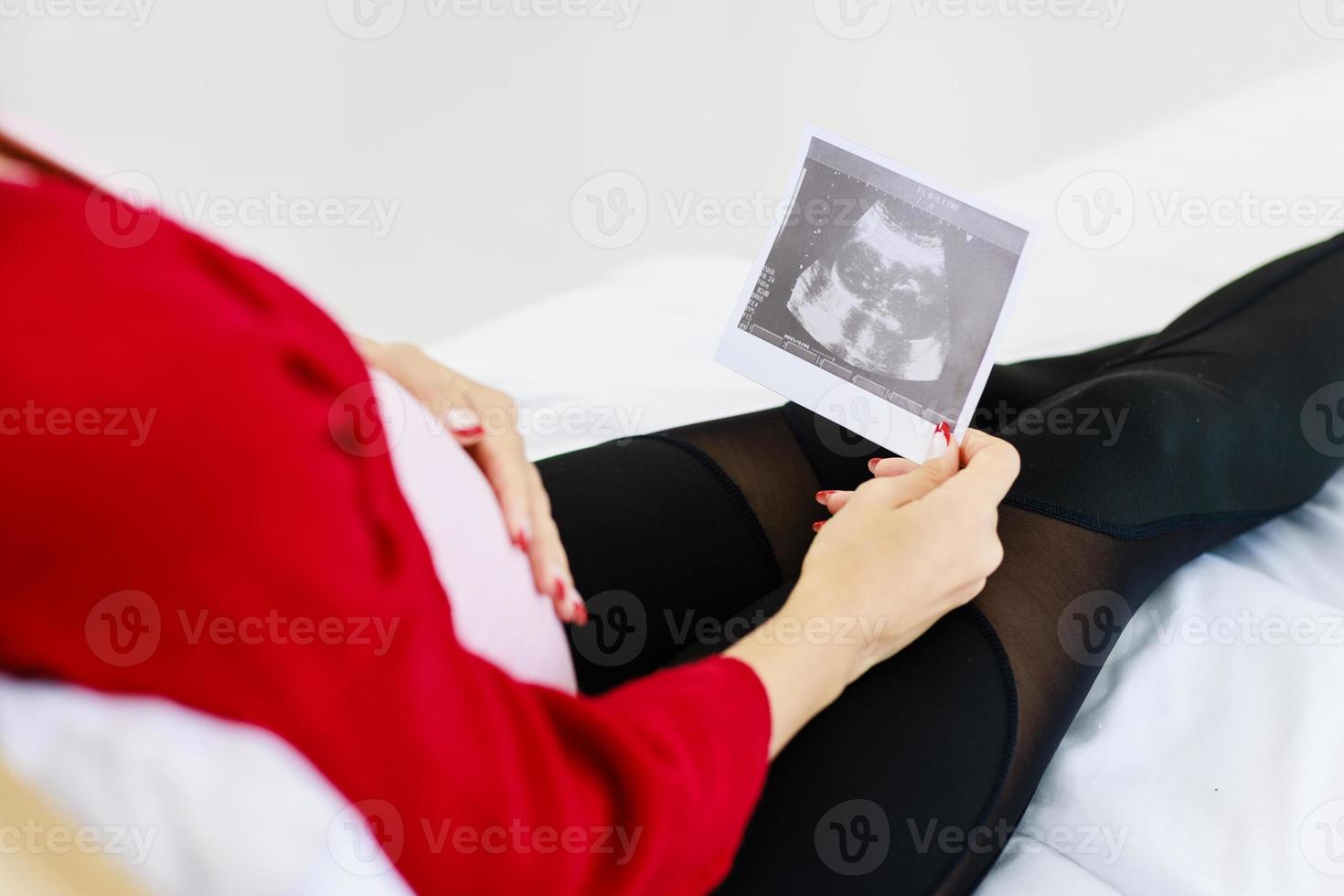 Beautiful caucasian mother happily and excitedly holding ultrasound images on her bed in her bedroom photo