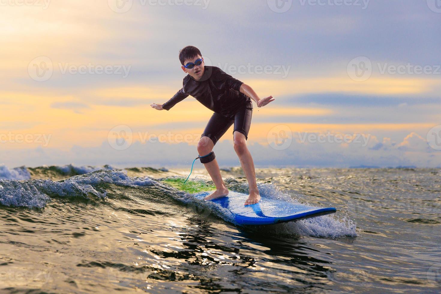 Young boy kid surfer riding waves with  soft board in Rayong beach, Thailand. Rookie surfboard student playing on water in excited face and funny action. photo