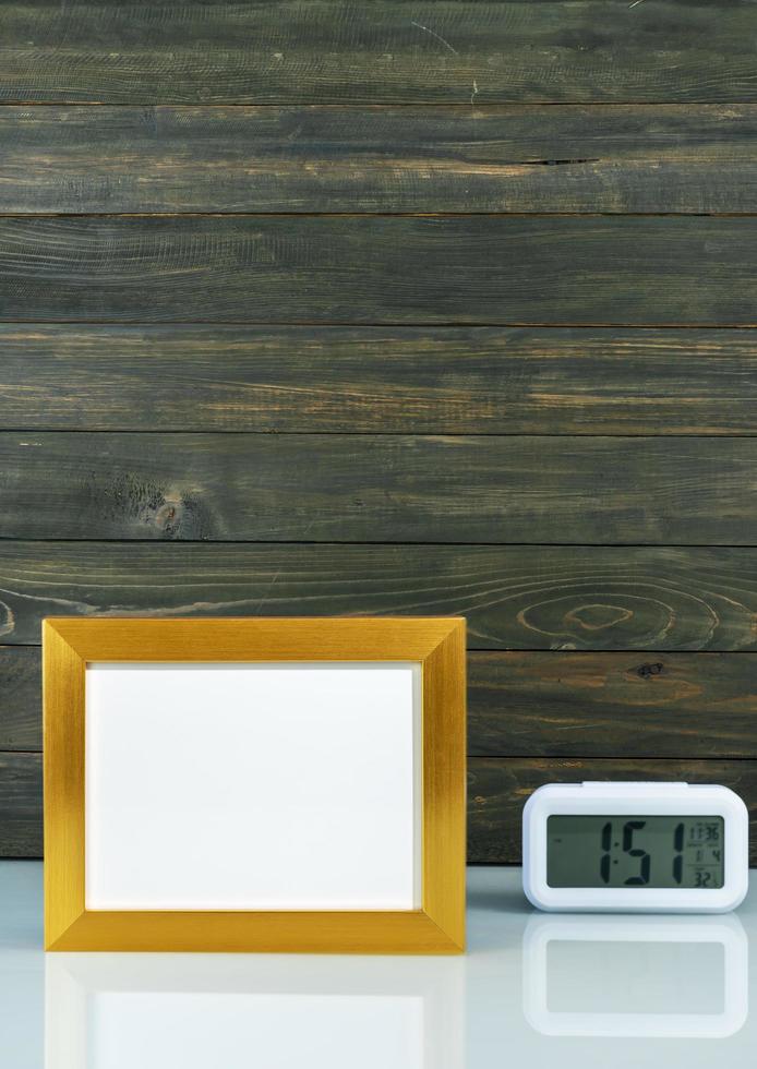 Blank golden frame and digital alarm clock on table photo