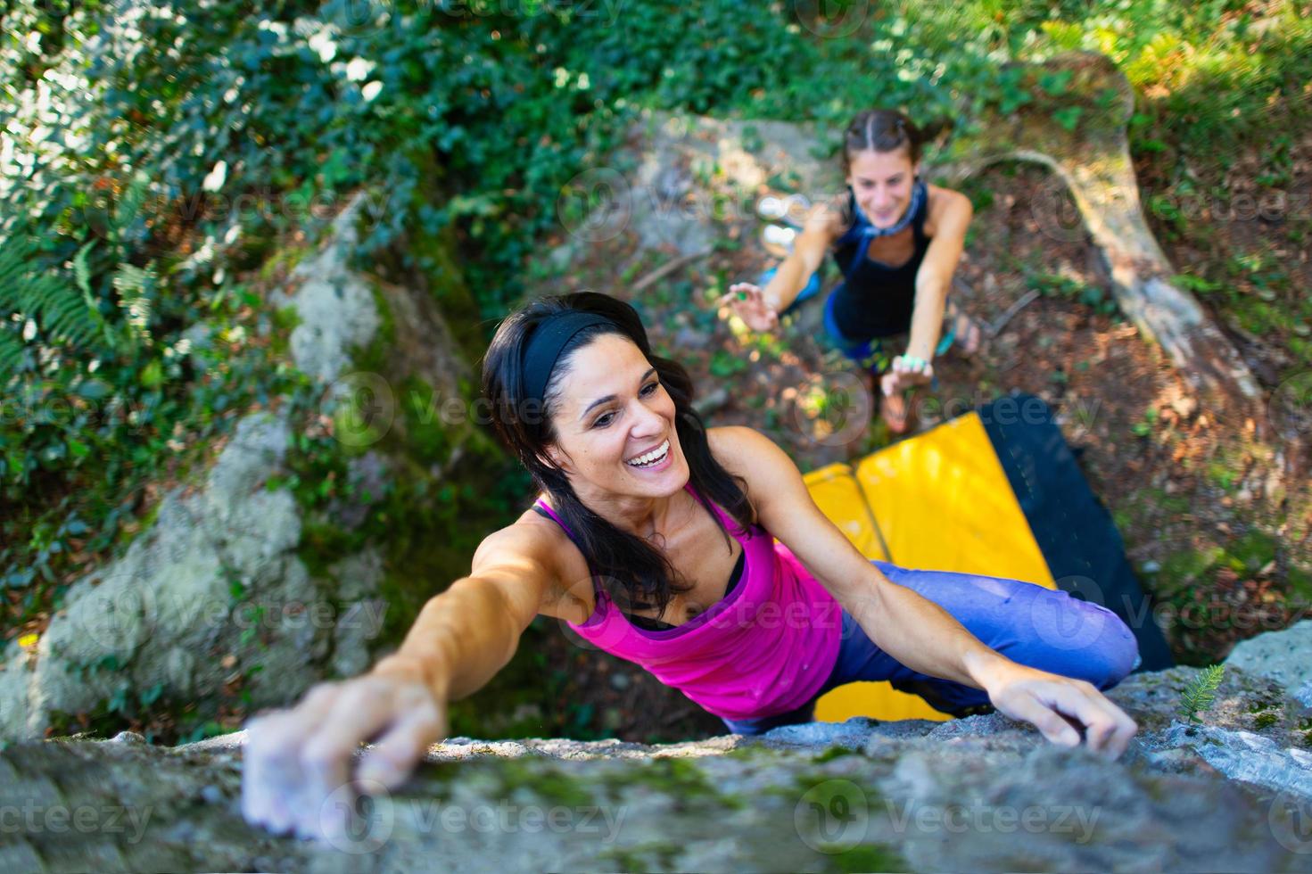 niña feliz practicando boulder con la plataforma de choque y su pareja protegiéndola en caso de caída foto