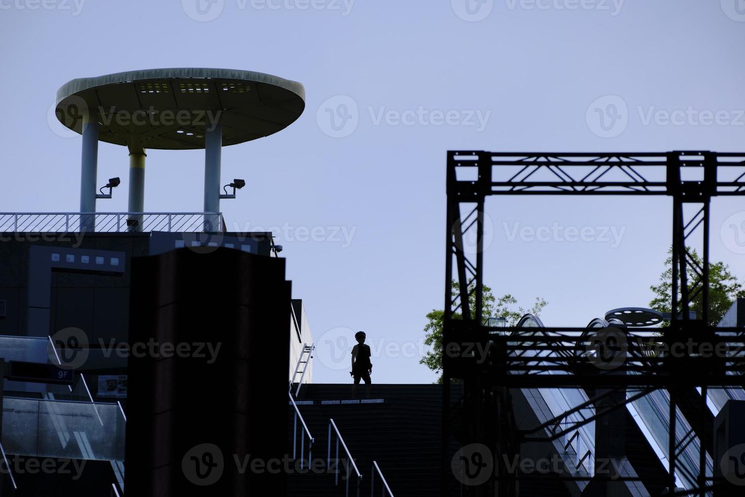 A boy in silhouette waits at the top of a staircase at the top of Kyoto Station photo