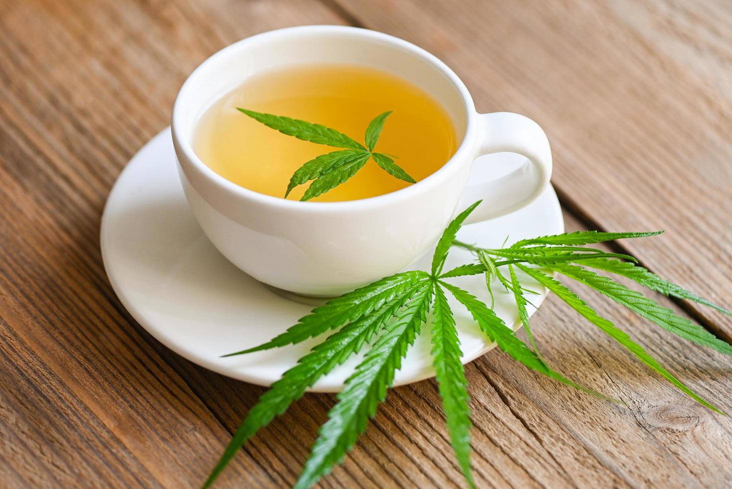 té de cannabis a base de hierbas en una taza de té con hoja de cannabis hojas de marihuana hierba sobre fondo de madera, té de salud con planta de hoja de cáñamo thc cbd hierbas comida y concepto médico foto